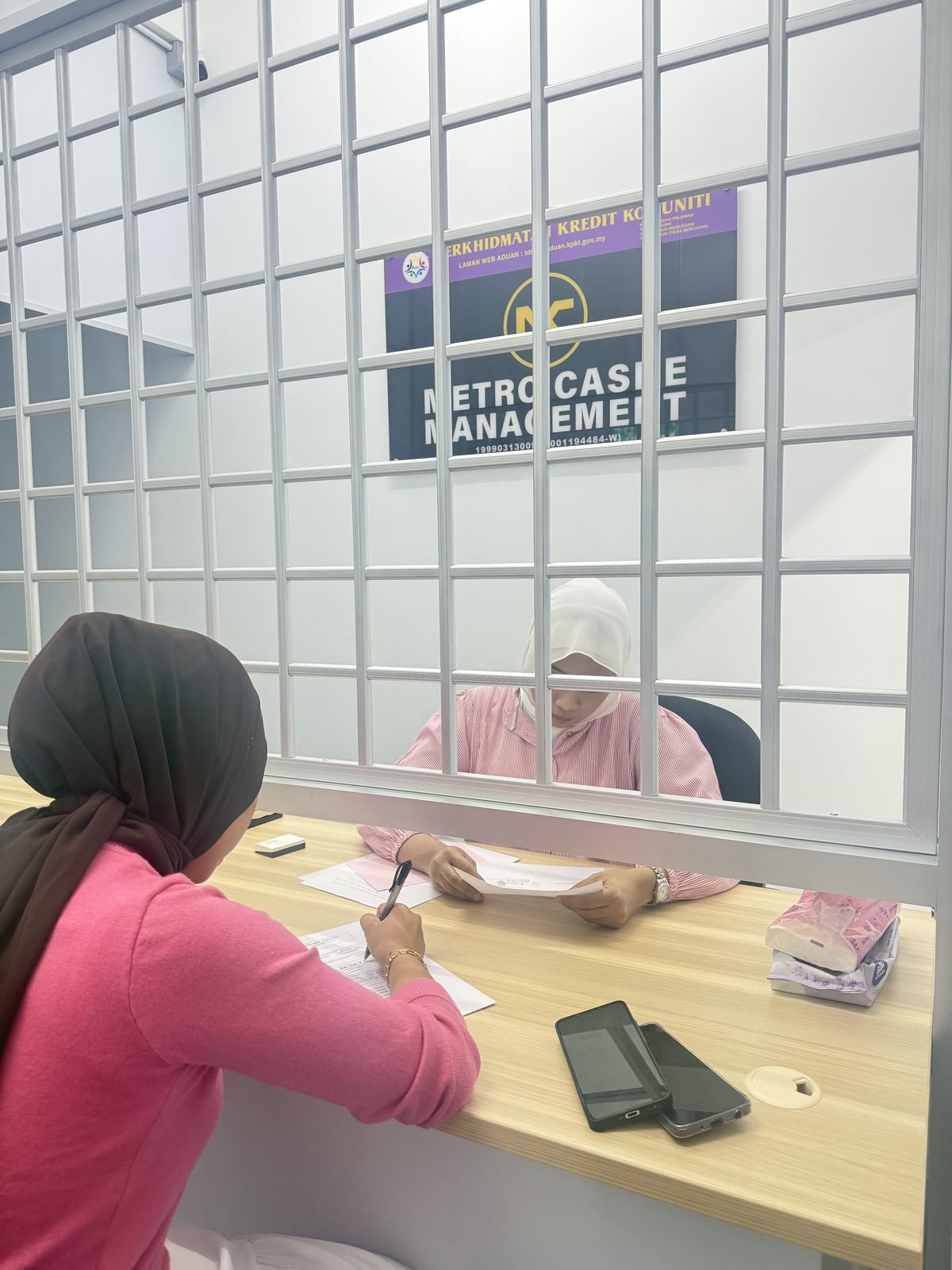 A Metro Cashe Management officer serving a customer at the counter, with the company signboard on the wall behind